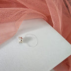 Silver earring on a white display card with pink fabric in the background