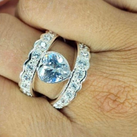 A sterling silver ring with a heart-shaped cubic zirconia at its center, featuring a double band design on a person's finger.