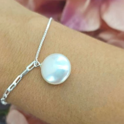 A sterling silver bracelet featuring a coin pearl as the central charm, displayed on a person's wrist.