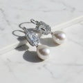 Pearl earrings with green gemstones on a gray background