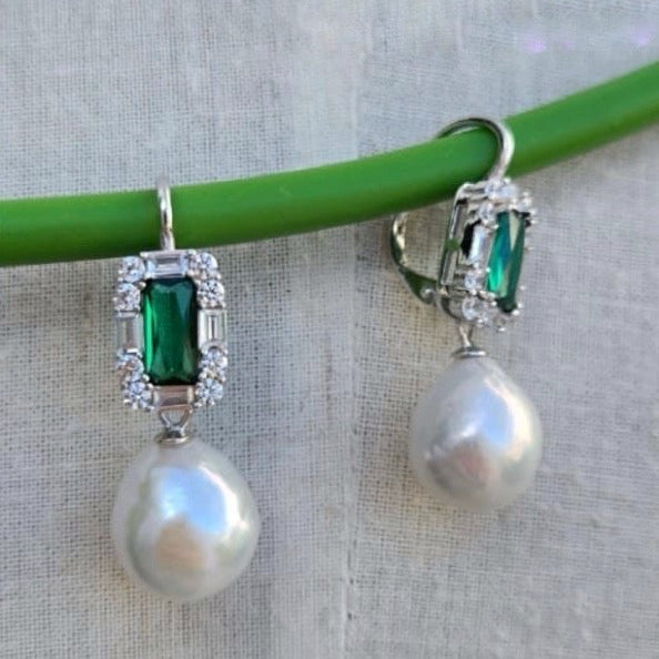 Pearl earrings with green gemstones on a gray background