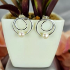 A pair of modern double circle earrings with freshwater pearls, displayed in a white pot with green leaves.