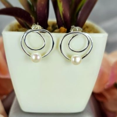 A pair of modern double circle earrings with freshwater pearls, displayed in a white pot with green leaves.