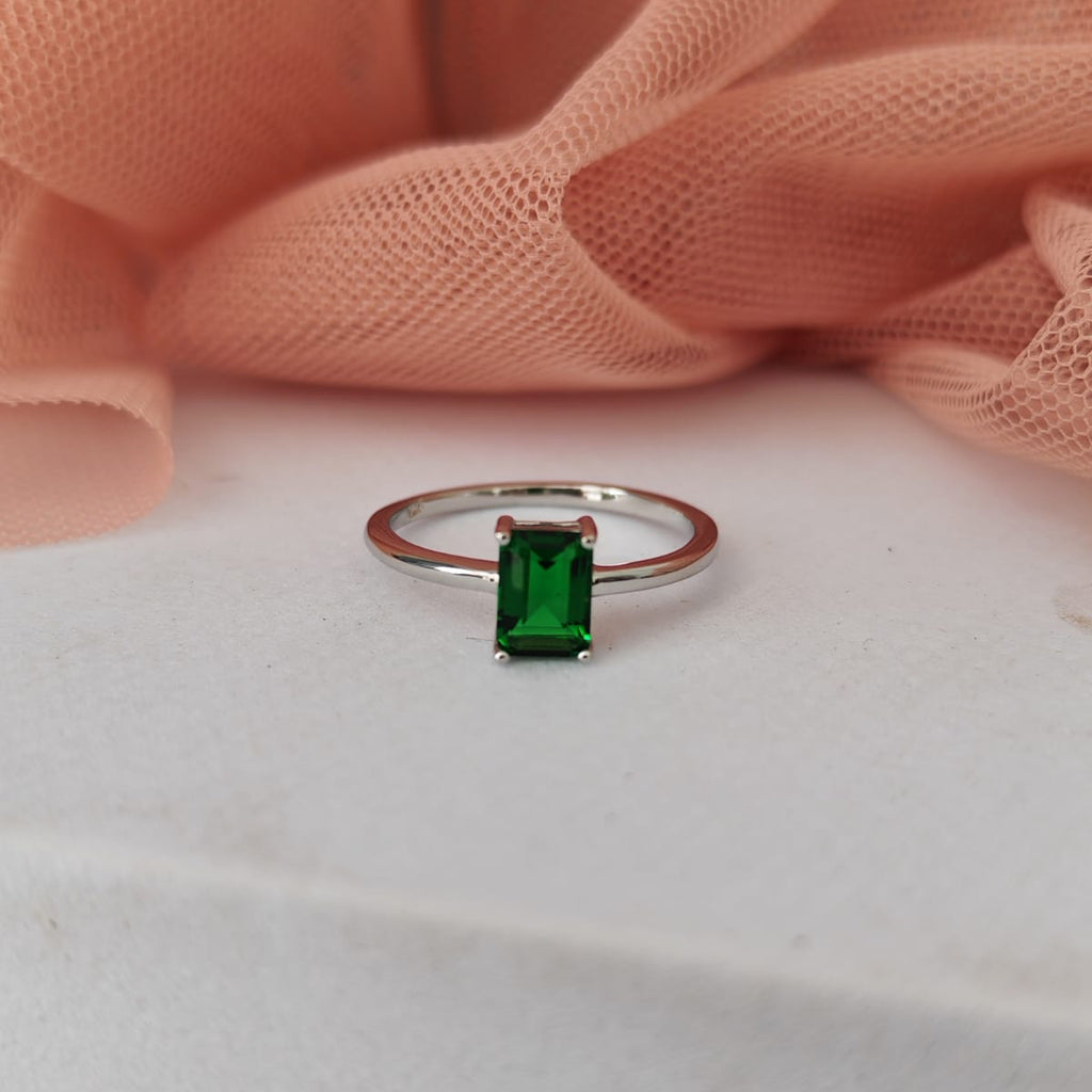 Ring with a green gemstone on a white surface with pink fabric in the background