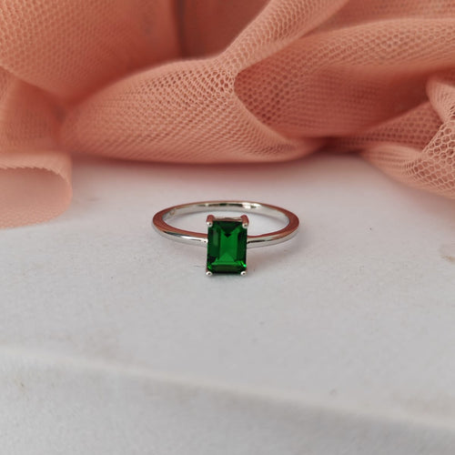 Ring with a green gemstone on a white surface with pink fabric in the background