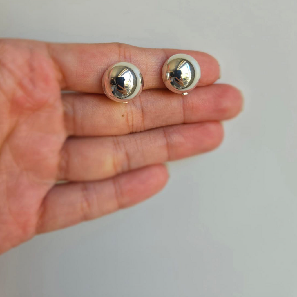A pair of sterling silver clip-on earrings with a ball design, held in a person's hand.