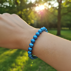 A blue freshwater pearl bracelet displayed on a person's wrist with a floral background.