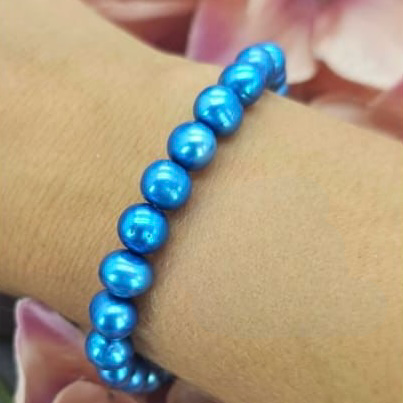 A blue freshwater pearl bracelet displayed on a person's wrist with a floral background.