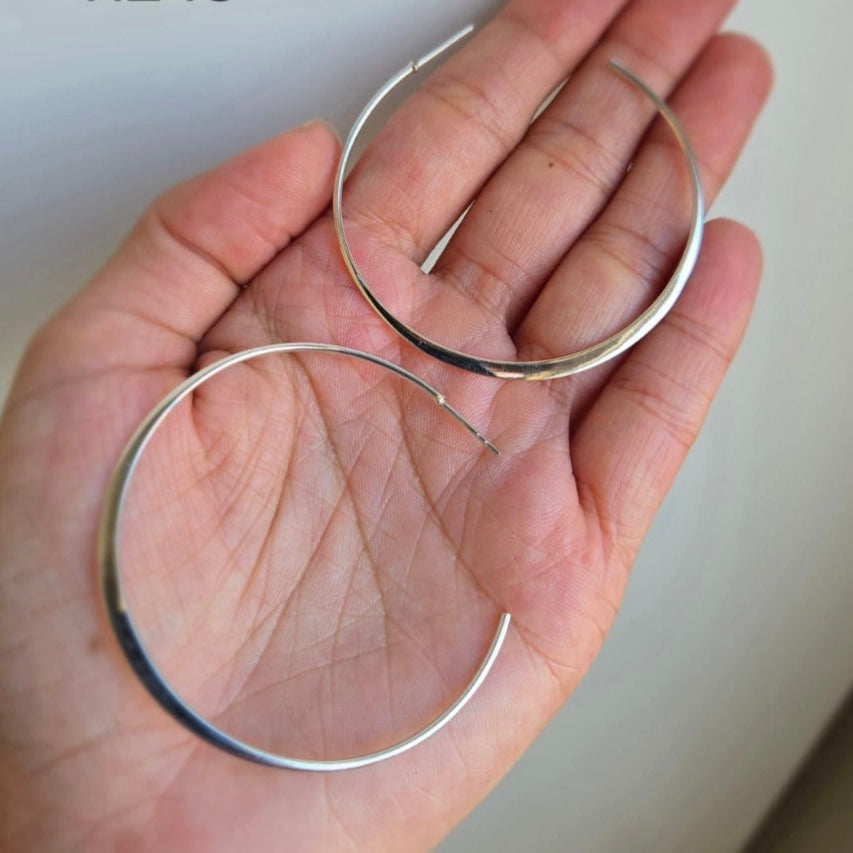 Two large silver hoop earrings with a butterfly design are displayed, held in a person's hand.