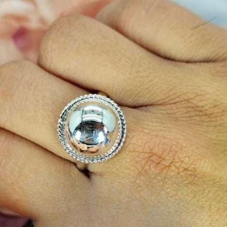 A sterling silver ring with a large 17mm ball and riffle detail on the edge, displayed on a person's finger.