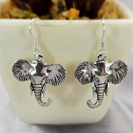 A pair of sterling silver drop earrings designed to resemble elephants, displayed in a white container with a green plant background.