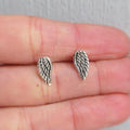 Silver angel wing earrings on a person's hand with a neutral background