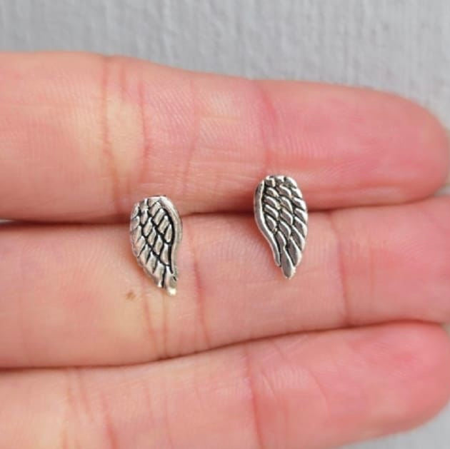 Silver angel wing earrings on a person's hand with a neutral background