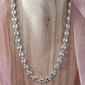 Silver chain necklace on a wooden surface with pink fabric in the background