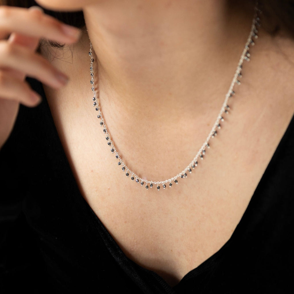 A person wearing a sterling silver necklace with hematite semi precious stones dangling on it.