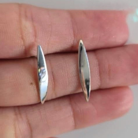 Silver earrings held between fingers on a neutral background
