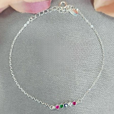 A silver bracelet with rainbow-colored cubic zirconia stones, displayed on a grey surface with a pink flower in the background.