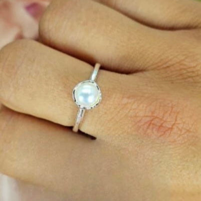 An adjustable sterling silver ring with a freshwater pearl in a clasp setting, displayed on a person's finger.