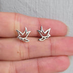 Silver bird-shaped earrings on a person's finger against a neutral background
