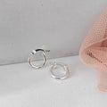 Silver hoop earrings on a light gray surface with a pink mesh fabric in the corner.