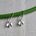 Silver bee-shaped earrings hanging from a green rod on a gray fabric background