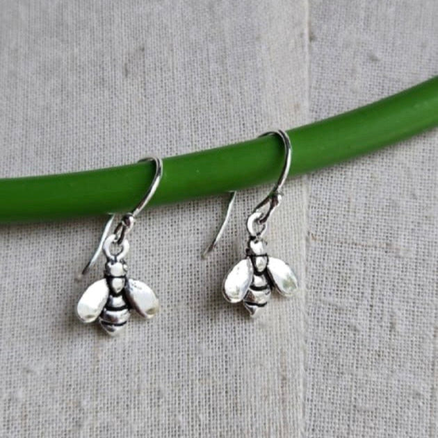 Silver bee-shaped earrings hanging from a green rod on a gray fabric background