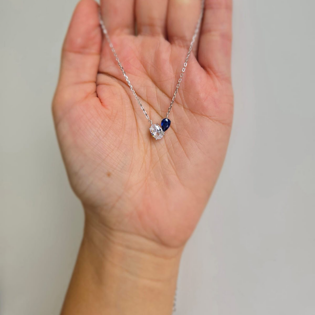 A hand holding a blue and white cubic heart-shaped necklace with a silver chain.