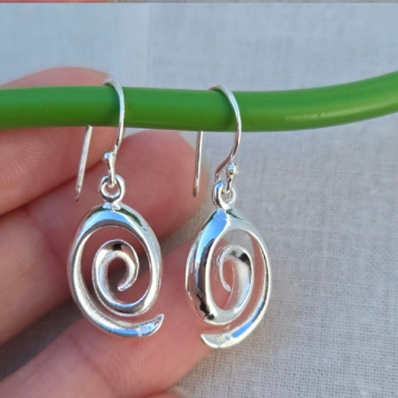 Silver spiral earrings held by a hand against a neutral background