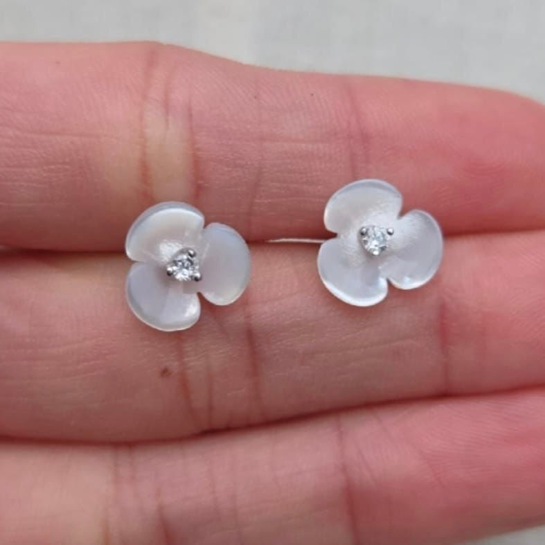 Flower-shaped earrings with clear stones held between fingers on a light background