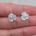 Flower-shaped earrings with clear stones held between fingers on a light background
