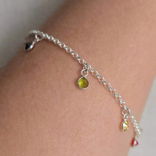 Silver anklet with yellow beads on a person's ankle against a neutral background