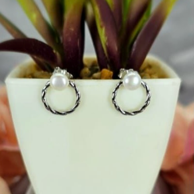 A pair of sterling silver round stud earrings with freshwater pearl tops, displayed in a white pot with green leaves.