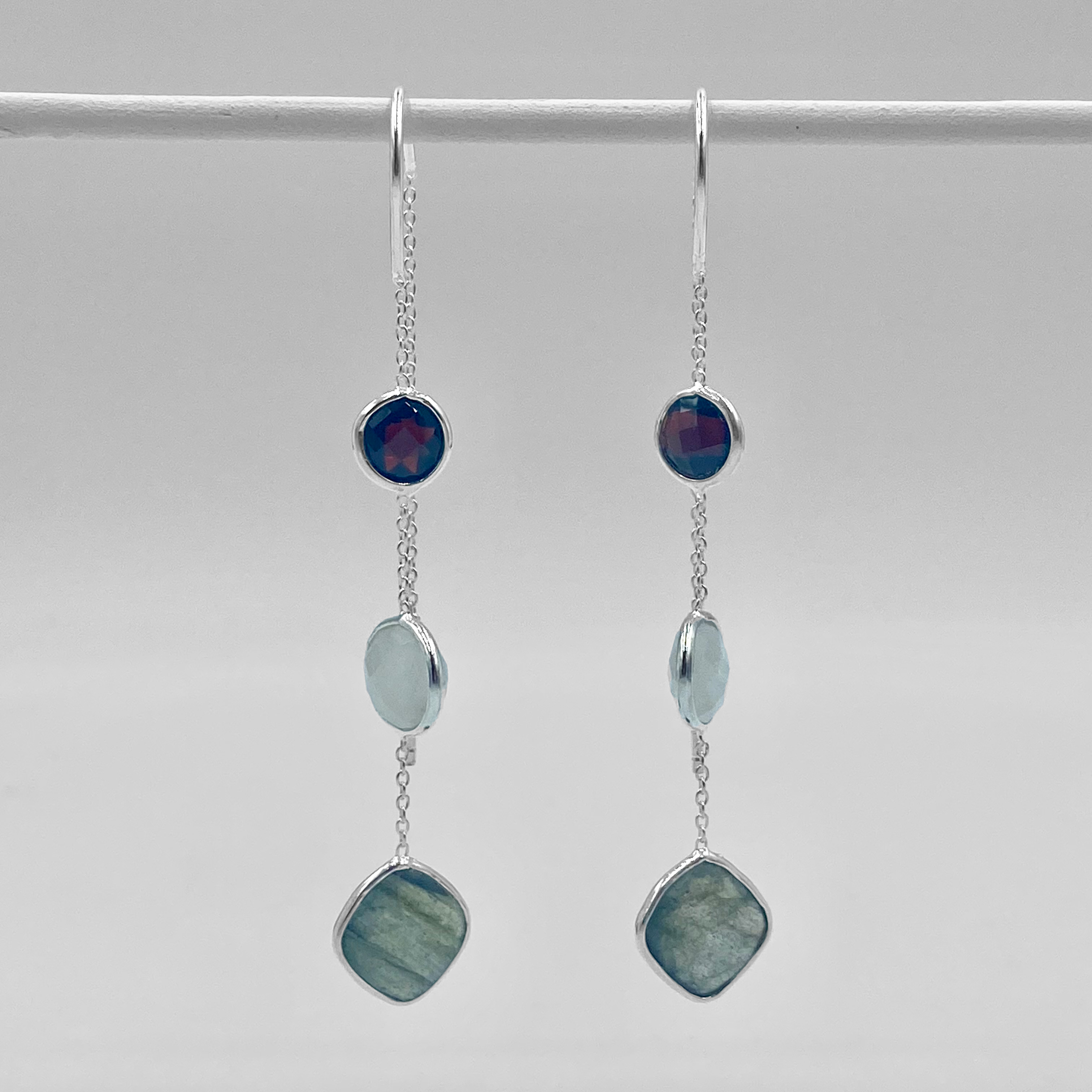 A pair of sterling silver drop earrings with moonstone, garnet, and lab chain.