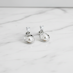 A pair of sterling silver drop earrings with cubic zirconia stud tops, displayed in a white vase with a green plant in the background.