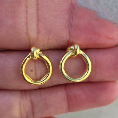 Gold hoop earrings held between fingers against a neutral background