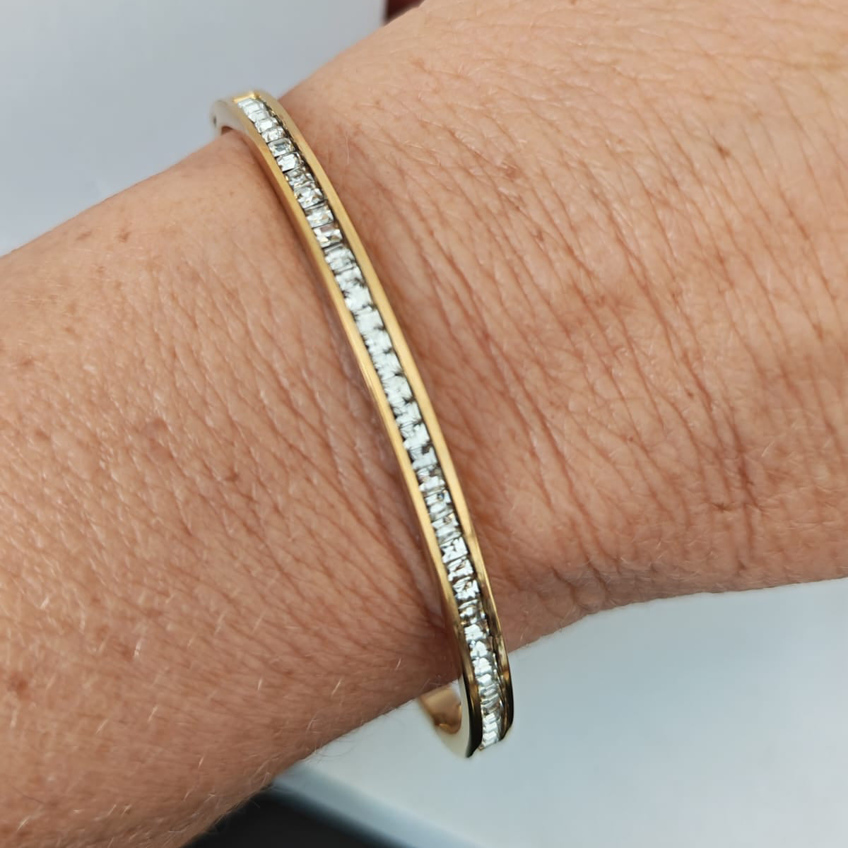 Gold bracelet with diamonds on a wrist against a neutral background