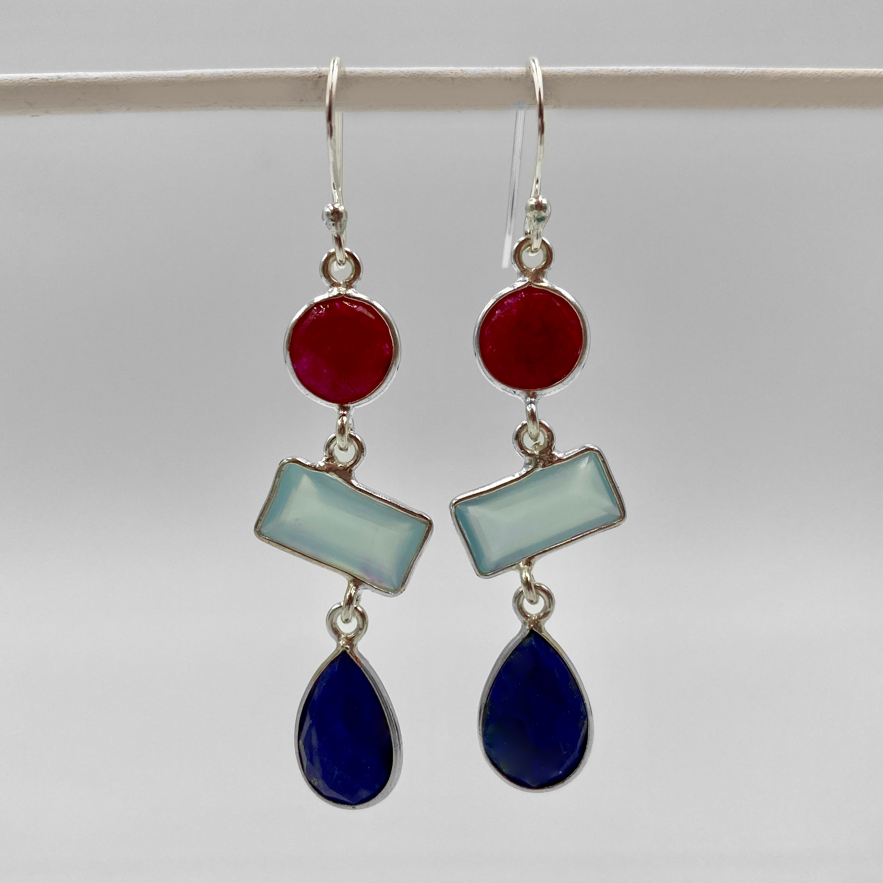 A pair of semi precious stone 3 layer drop earrings with ruby, lapis, and aquamarine colors, suspended from sterling silver hooks.