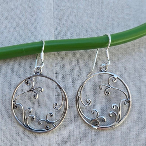 Silver earrings with intricate designs hanging on a green rod against a light background