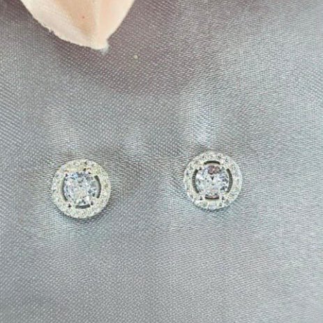 Round silver earrings with clear gemstones on a gray fabric background