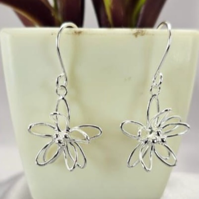 A pair of sterling silver flower drop earrings displayed on a flat surface next to a potted plant.