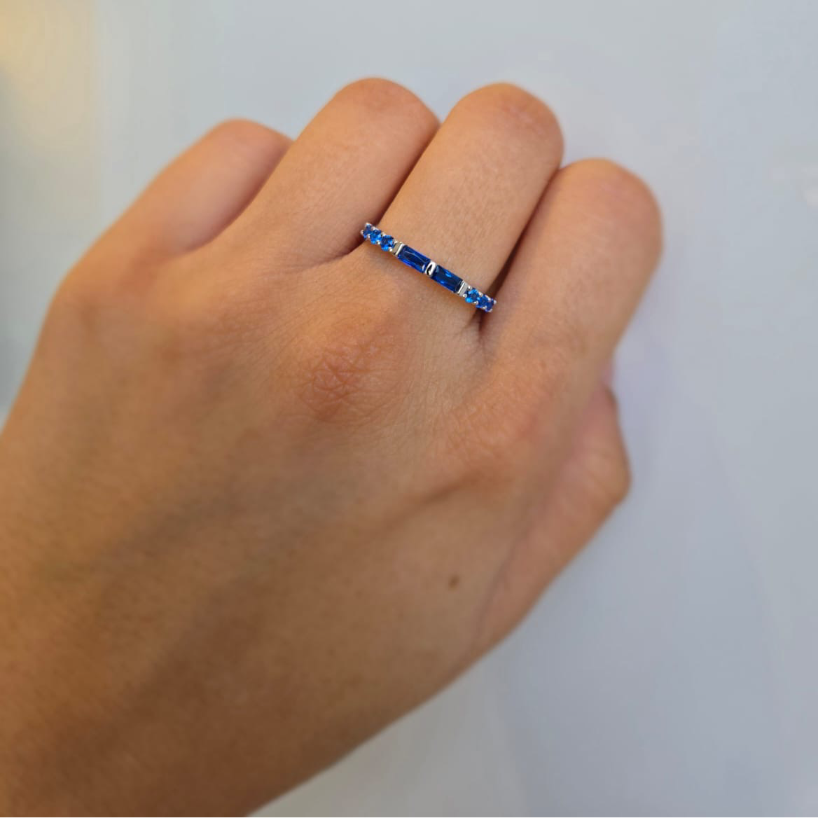 A hand wearing a sterling silver ring adorned with blue cubic zirconia stones.