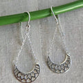 Silver earrings hanging from a green rod on a textured gray background