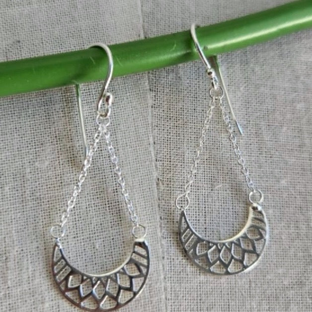 Silver earrings hanging from a green rod on a textured gray background