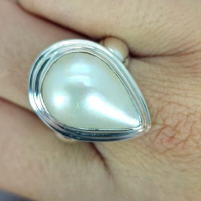 A teardrop freshwater pearl ring with a sterling silver setting, displayed on a person's finger.