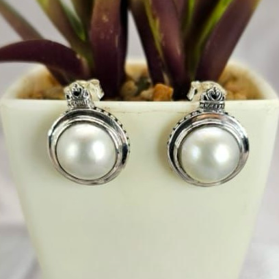 A pair of sterling silver Mabe pearl stud earrings displayed in front of a potted plant.