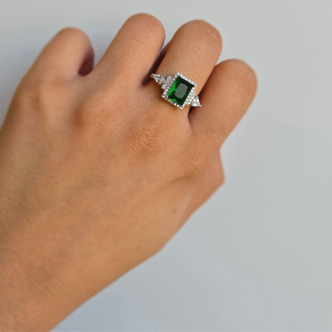 A sterling silver ring with a rectangular green cubic zirconia centerpiece and smaller white stones around it, displayed on a person's finger.