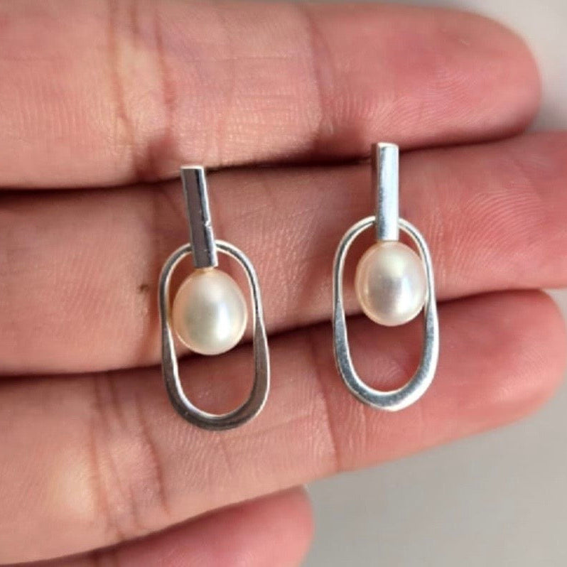 Silver earrings with pearl drops held between fingers