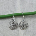Silver filigree earrings on a green wire against a gray fabric background