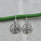 Silver filigree earrings on a green wire against a gray fabric background