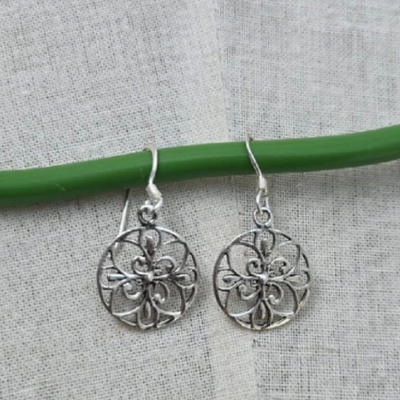 Silver filigree earrings on a green wire against a gray fabric background